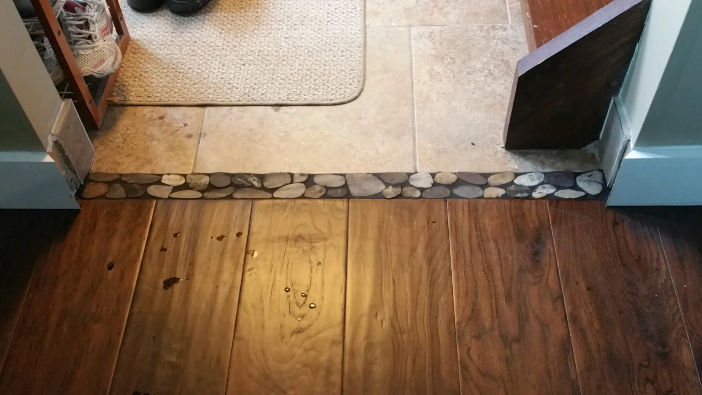 Hardwood to tile transition with a river-stone inlay installed by JD Flooring